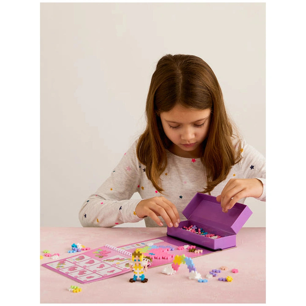 Plus Plus Fairytale Activity Pad displayed on a white table with a girl, pink box, and Lego toy in a lifestyle scene.