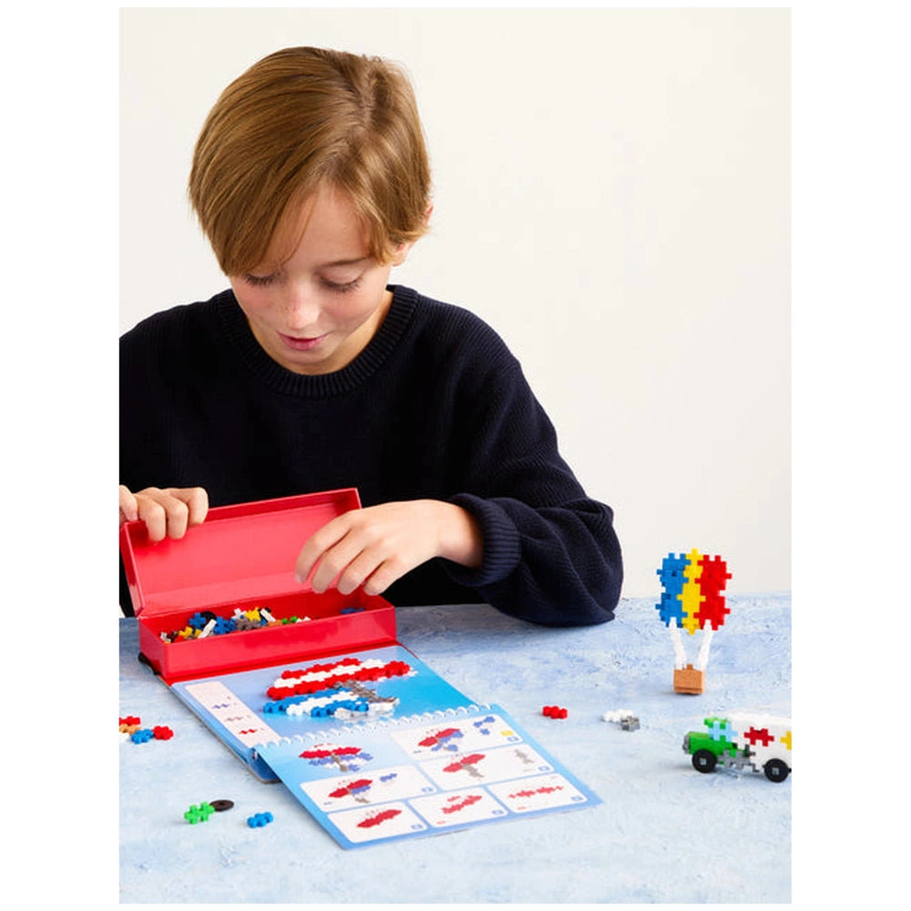 Plus Plus Transportation Activity Pad puzzles on a light blue table with a child in a dark blue shirt and sweater engaged in 