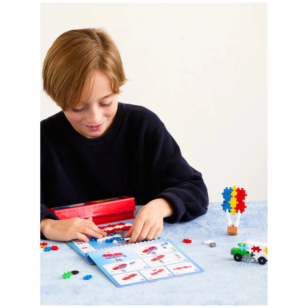 Plus Plus Transportation Activity Pad in a red box with a glossy lid, featuring a green toy car on a blue tablecloth.
