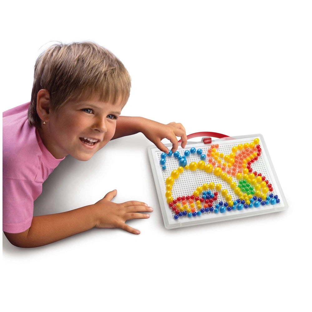 Quercetti FantaColor Portable features a smiling child in a pink shirt arranging colorful plastic beads on a white bead board