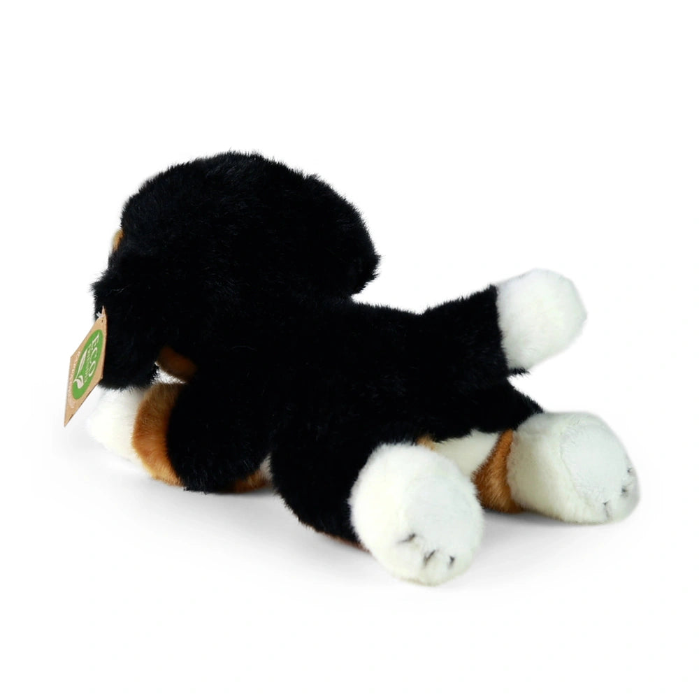 Plush Bernese mountain dog toy with black and white fur, featuring a brown paper tag with a green logo.
