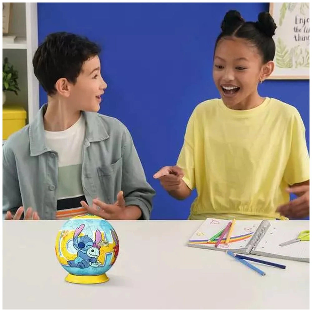 Ravensburger 3D Puzzle Ball featuring Disney's Stitch is being enjoyed by two smiling children at a table with craft supplies