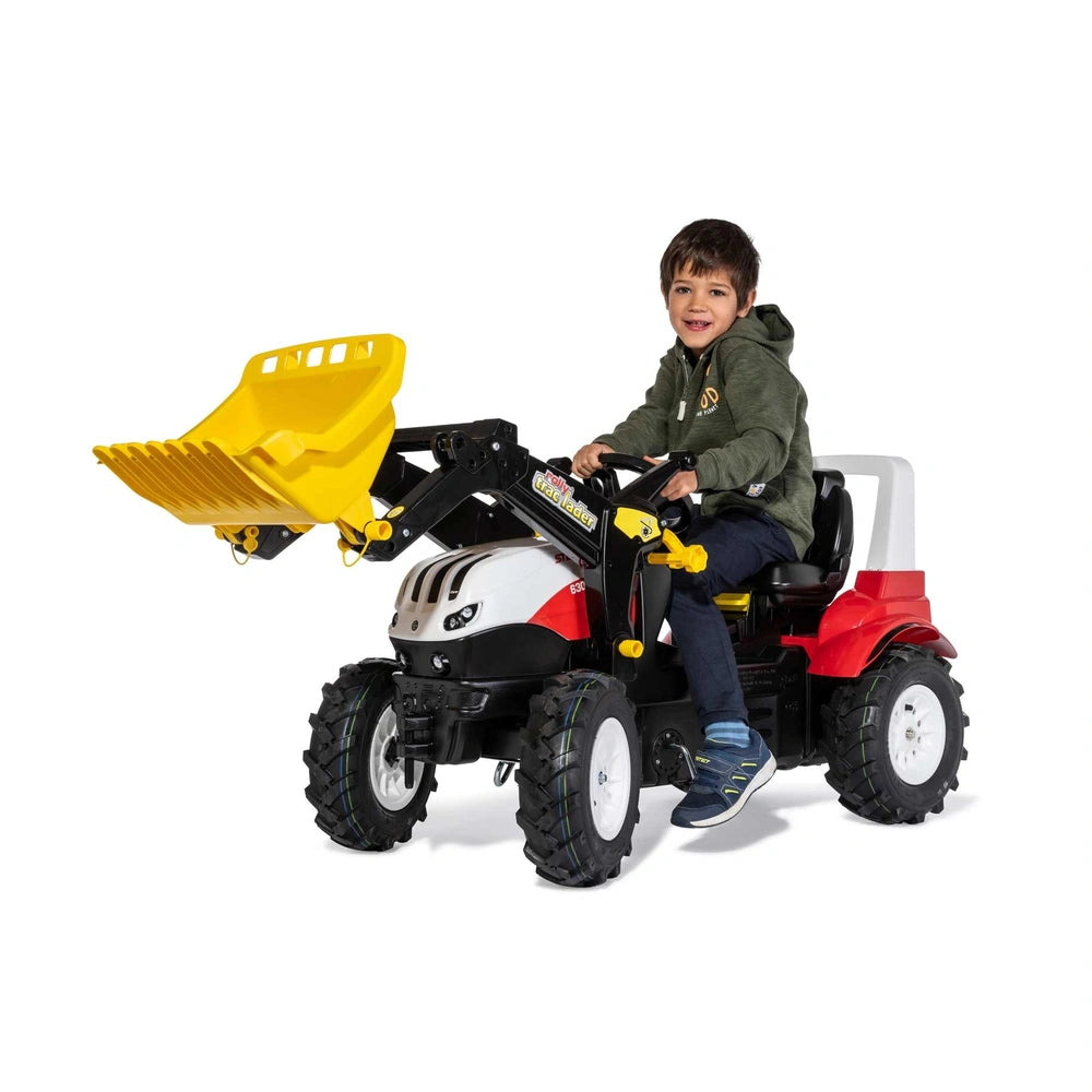 Rollyfarmtrac Premium II Steyr 6300 Terrus CVT toy vehicle with a smiling child in a dark hoodie and blue shoes.