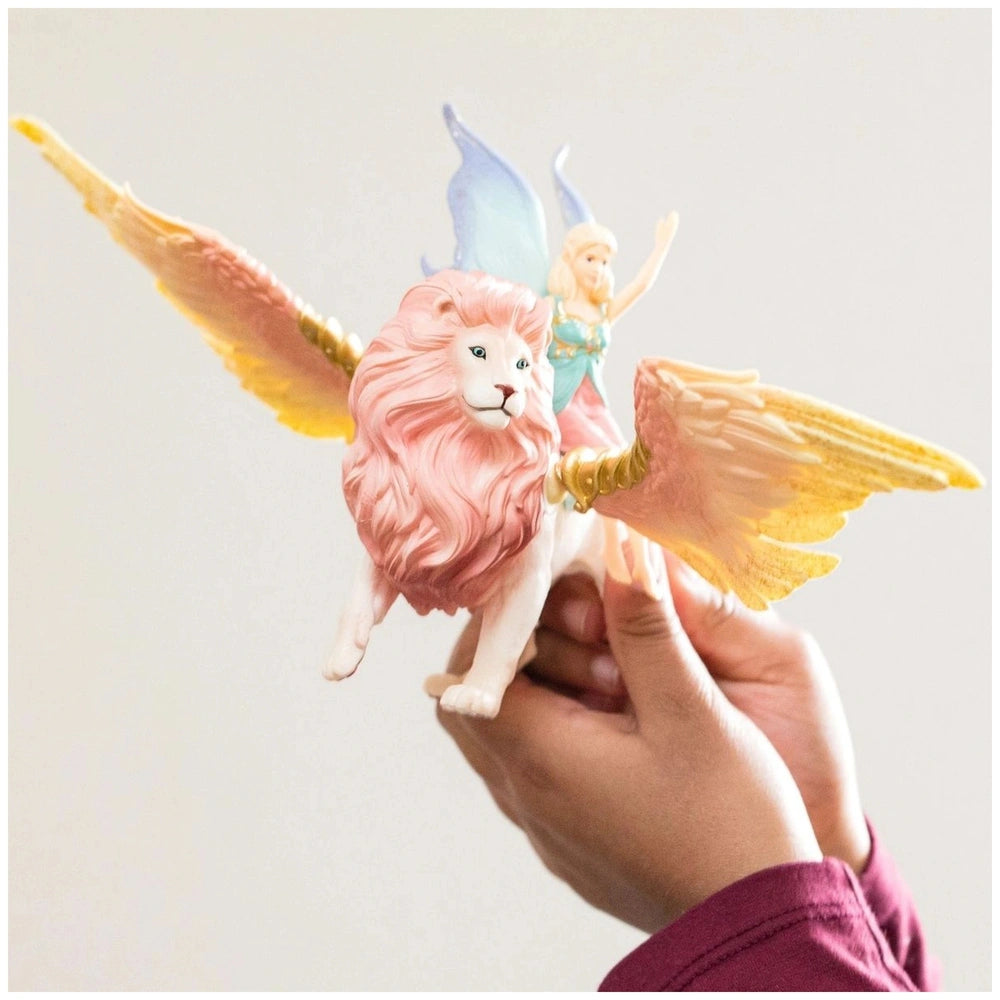 Schleich Bayala fairy in flight on a pink winged lion, featuring translucent yellow wings and a smiling feminine figure.