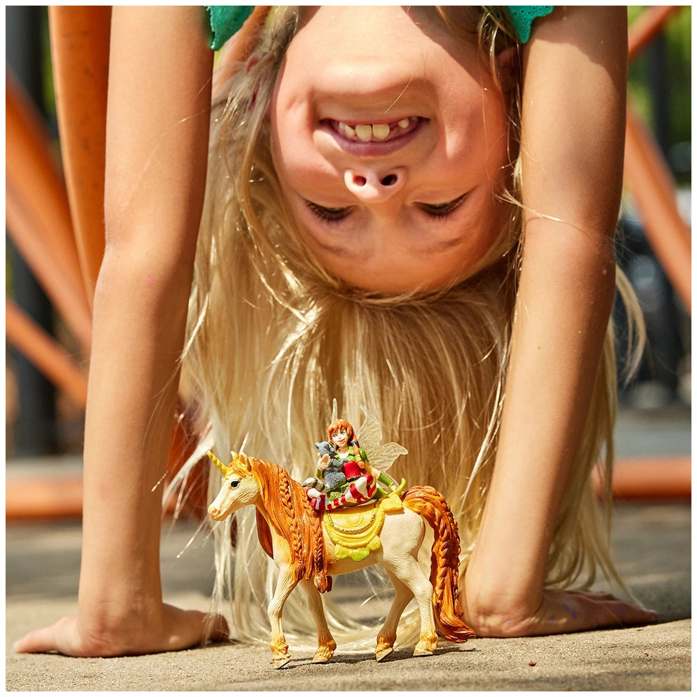 Fairy Marween figurine is held by a smiling girl upside down on a gray concrete surface, showcasing joy and playfulness.