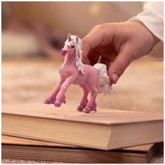 Flower Unicorn Foal toy horse with pink body and white fuzzy mane, held by a hand in a close-up lifestyle scene.