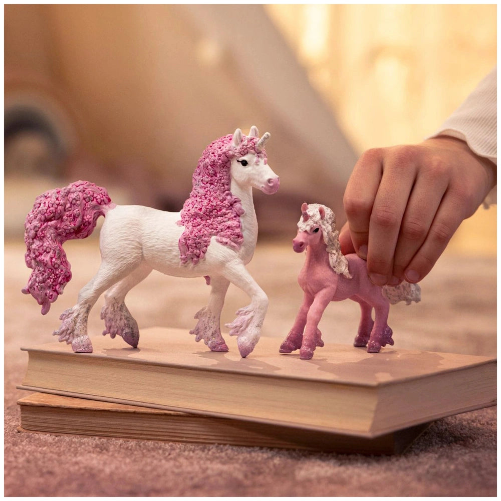 Schleich Flower Unicorn Foal toy figures feature two white and pink unicorns with pink manes and hooves on a brown surface.