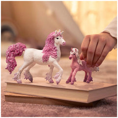 Schleich Flower Unicorn Foal toy figures feature two white and pink unicorns with pink manes and hooves on a brown surface.