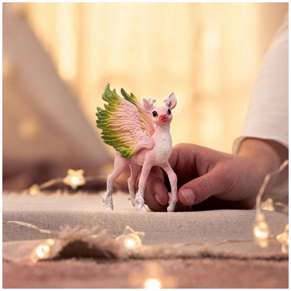 Magical Fawn figurine with pinkish-white skin and green wings held by a hand on a light brown surface.