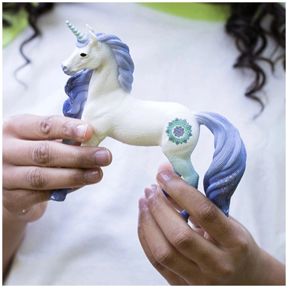 Mandala Unicorn Stallion figurine with a white body and blue mane, held delicately in a person's hands.