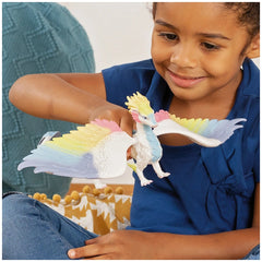 Blue-shirted girl interacts with a colorful plastic Rainbow Dragon toy on a patterned blue pillow.