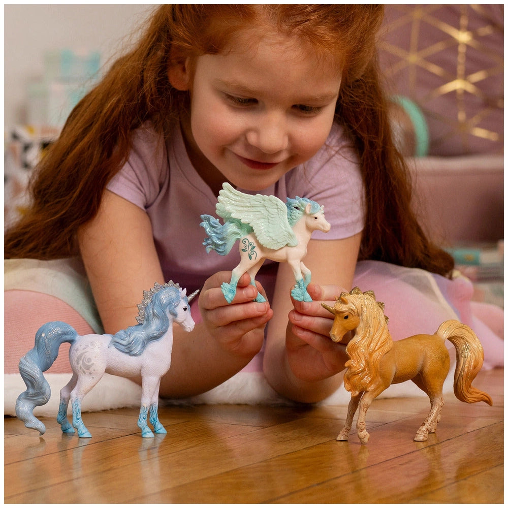 Schleich Stormy Unicorn Foal with red hair and purple shirt, surrounded by unicorns and horses on a light brown wooden floor.