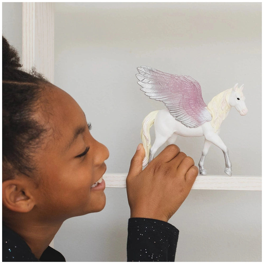Schleich Sunrise Pegasus toy figure with a young girl in a black glittery top and a white wall with horse artwork.