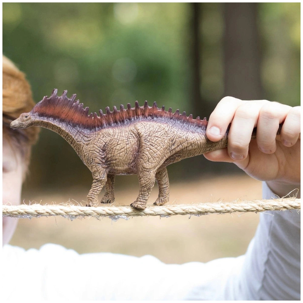 Amargasaurus dinosaur model with a long neck and spiky back held in a person's hand against a blurred green outdoor backgroun
