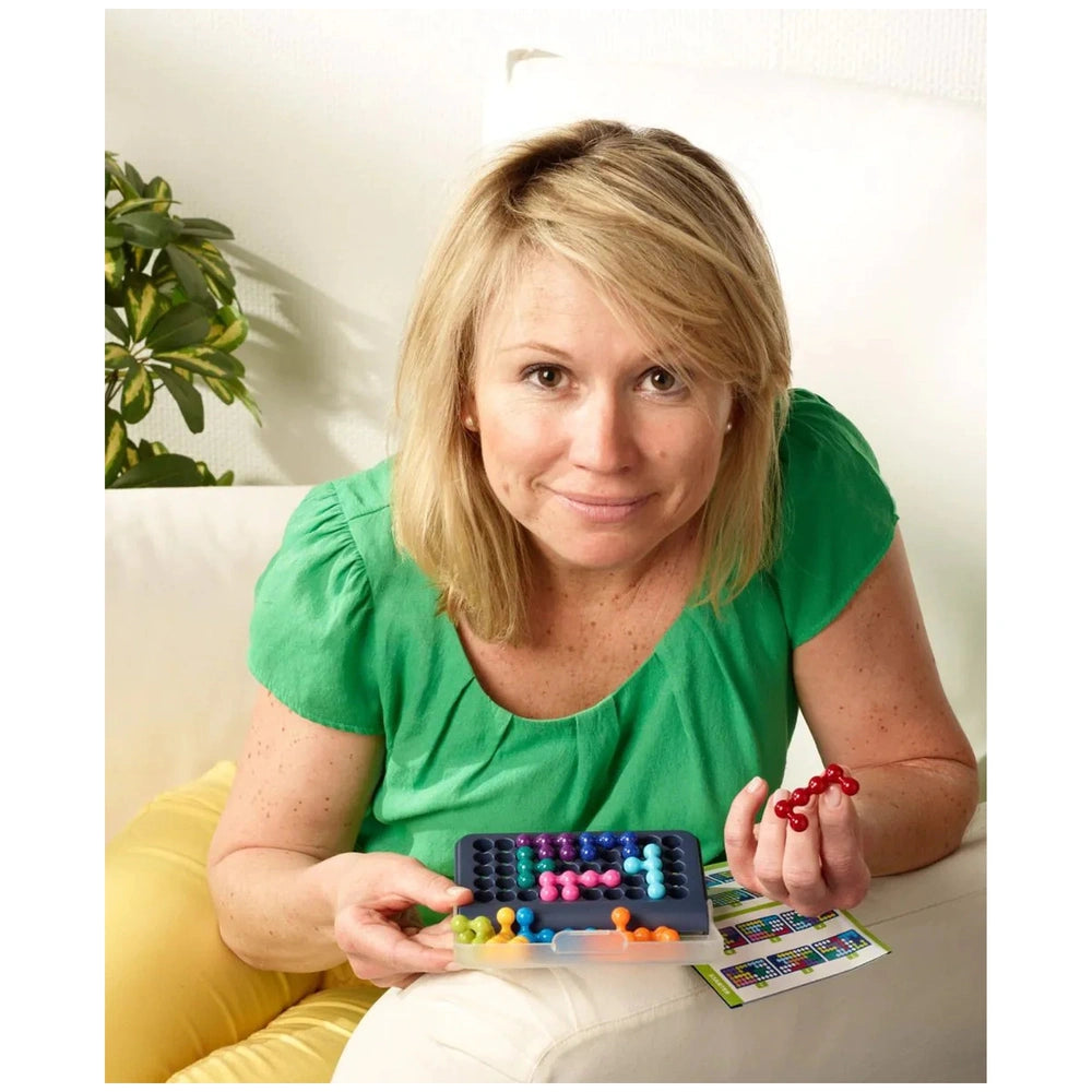 Smart Games IQ Fit logic puzzles are showcased as a woman in a green top holds a container of colorful beads on a couch.