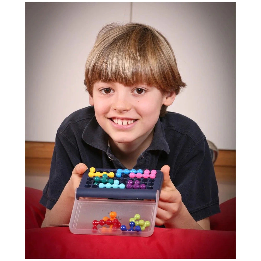 A young boy smiles while holding a container of colorful beads arranged in a grid, set against a neutral background.
