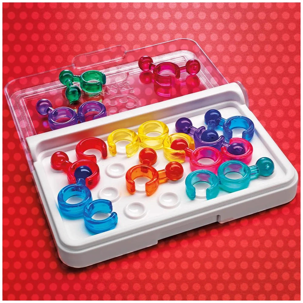 Smart Games IQ Link features colorful plastic rings and connectors arranged on a white tray atop a red polka-dotted surface.