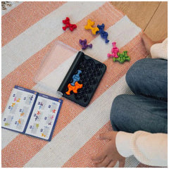 Smart Games IQ Waves logic puzzle set displayed on a black tray surrounded by colorful game pieces on the floor.