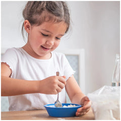Teifoc construction kit is showcased as a young girl smiles while holding a spoon over a bowl of food at a wooden table.