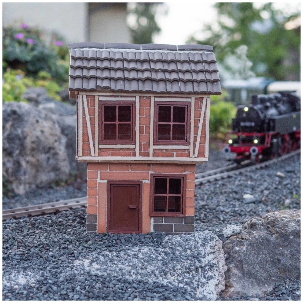 Teifoc Big Timber-framed house model set features a toy train on a track beside a small building with a red roof and gravel g