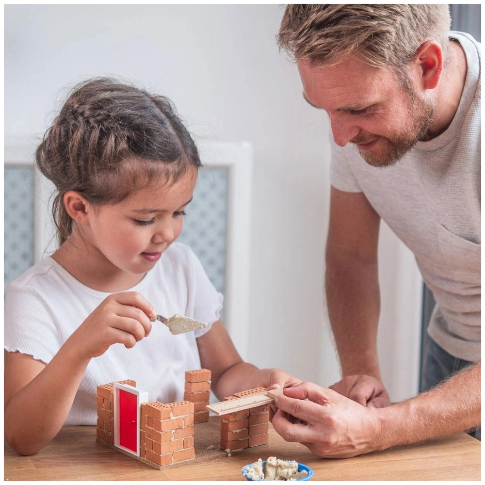 Teifoc Fire Station craft set being used by a man and a girl, focused on building with red bricks at a wooden table.