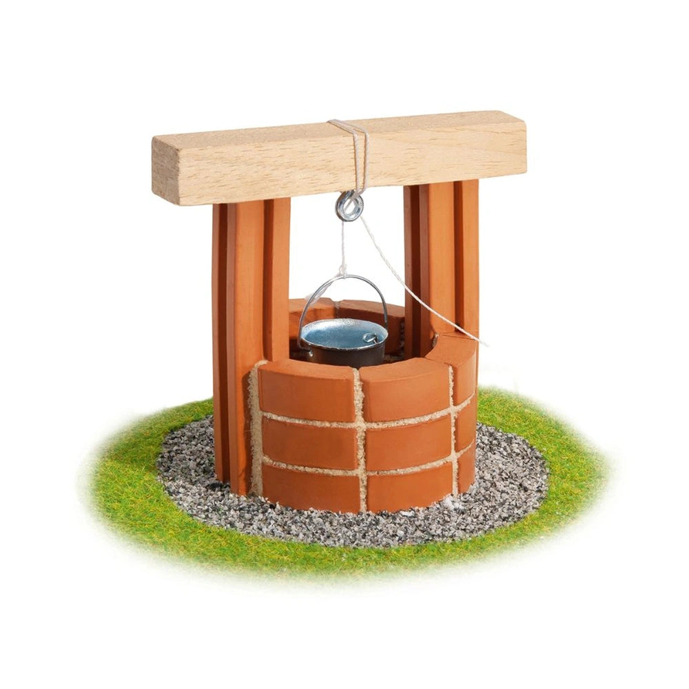 Teifoc well model with a brown wooden structure, glass bowl, rope, and gravel base, surrounded by green grass.