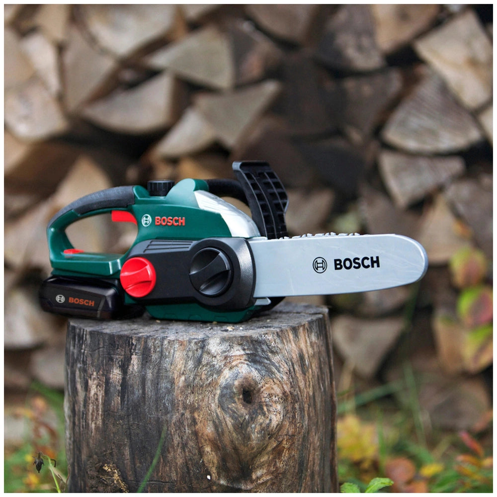 Theo Klein Bosch chainsaw in green and black on a wooden stump, featuring a metal blade and red button.