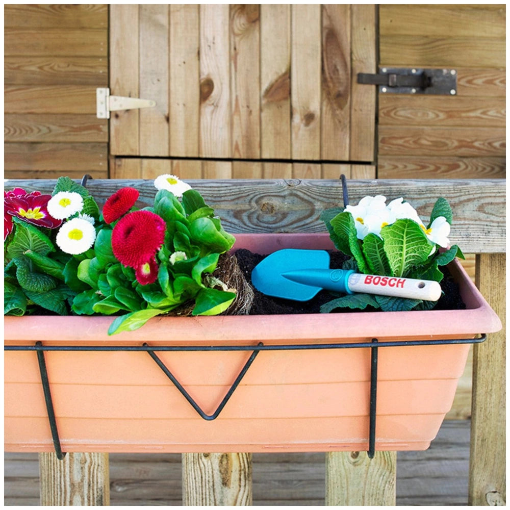 Theo Klein Bosch garden hand shovel in blue beside a pink container with green plants and red and white flowers.