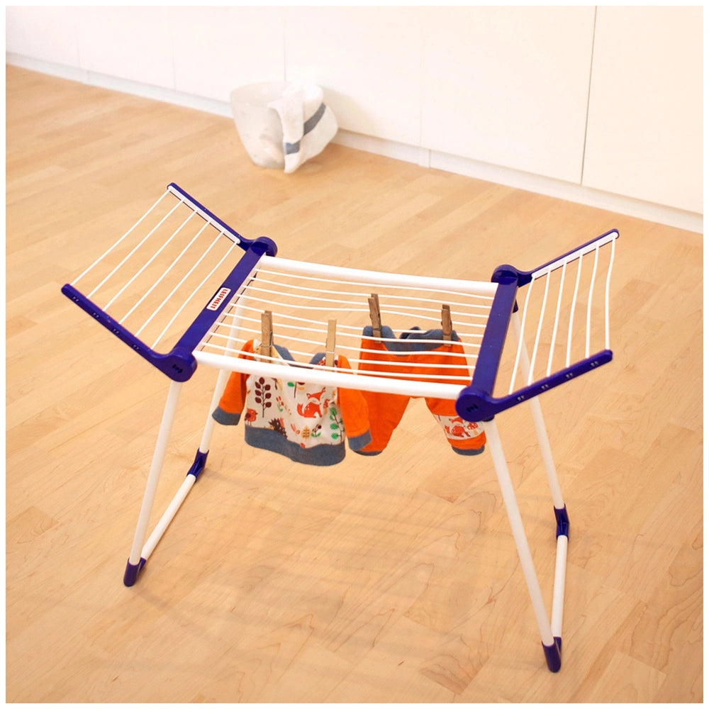 Theo Klein drying rack in white and blue plastic with clothes hangers displaying clothes, set on a wooden floor.
