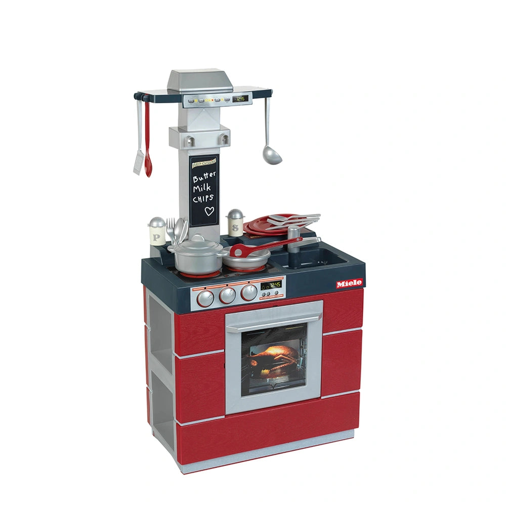 Theo Klein Miele Kitchen Compact features a red and black oven with silver cooking utensils and a gray countertop.